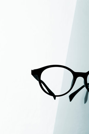 Closeup of a pair of black eyeglasses on a reflecting surface against a white