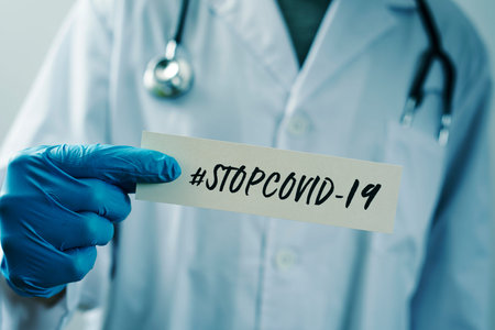 closeup of a doctor man, wearing blue surgical gloves, showing the message #stopcovid-19 written in...