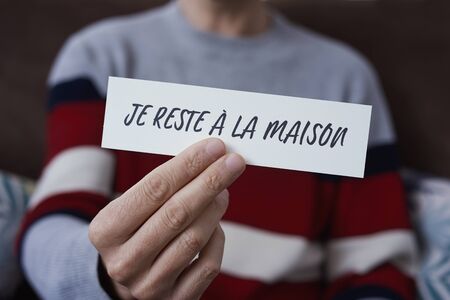 closeup of a man, in casual wear indoors, showing the message I stay at home in french written in a piece of paper, as a measure to stop the spreading of the covid-19の写真素材