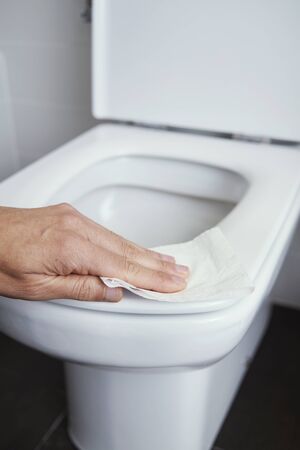 closeup of a caucasian man cleaning the toilet seat with a piece of toilet paper in a tiled bathroomの写真素材