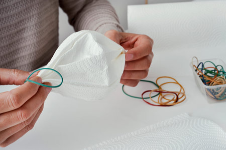 closeup of a caucasian man, sitting at a table, making a homemade face mask with paper towel and...