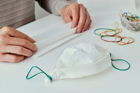 closeup of a caucasian man, sitting at a table, making a homemade face mask with paper towel and...