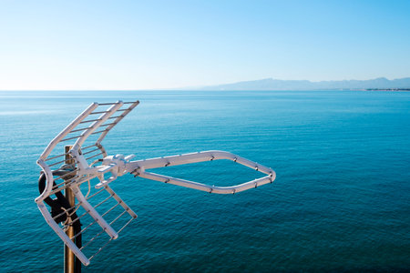Top section of a television antenna, with a calm sea and the blue sky