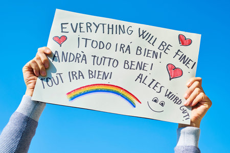 Man showing a homemade sign with the text everything will be fine in different languages