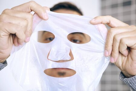 closeup of a caucasian man about to apply a bio-cellulose sheet mask to his own faceの写真素材