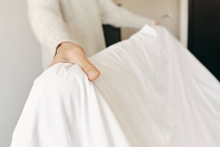 closeup of a young caucasian man making the bed with white bedsheetsの写真素材