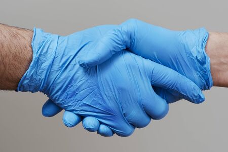 closeup of two people, wearing blue surgical gloves, shaking hands against a gray backgroundの写真素材