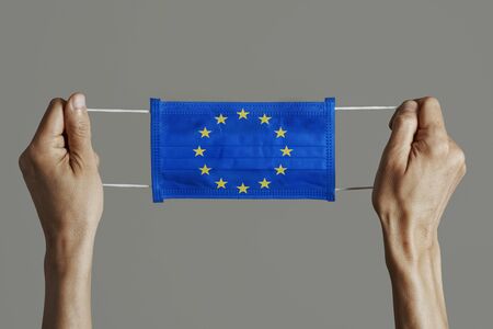 closeup of man holding a surgical mask patterned with the European flag on a gray backgroundの写真素材