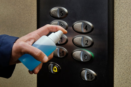closeup of a caucasian man disinfecting the buttons of an elevator, in an apartment building or...