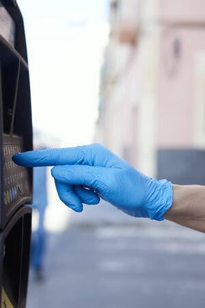 closeup of a young man, wearing blue latex gloves, using an electronic parking meter on the streetの写真素材
