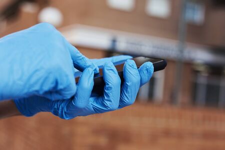 closeup of a young caucasian man on the street, wearing blue latex gloves, using his smartphoneの写真素材