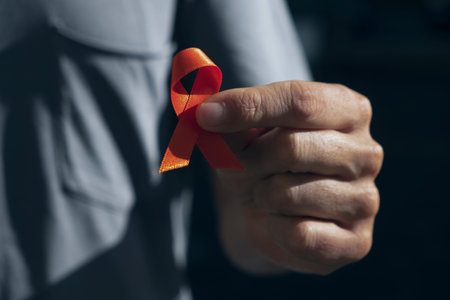 closeup of a young caucasian man with an orange ribbon in his hand, in support of people affected by...