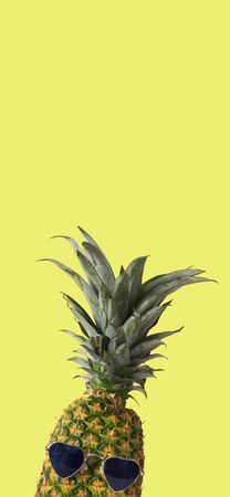 pineapple wearing heart-shaped sunglasses on a yellow background with some blank space on top, in a vertical format to use for mobile stories or as smartphone wallpaperの写真素材