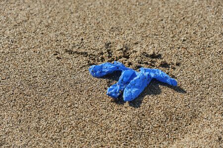 Closeup of a blue used latex glove thrown on the wet sand of the seashore of a beachの写真素材