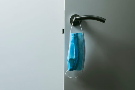 closeup of a blue surgical mask hanging on the modern doorknob of an open white door