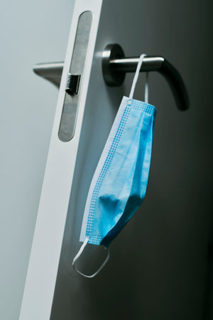 closeup of a blue surgical mask hanging on the modern doorknob of an open door