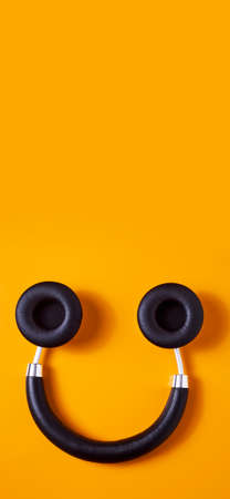 a pair of black wireless full size headphones upside down on an orange background, resembling a smiley face, in a vertical format to use for mobile stories or as smartphone wallpaperの写真素材