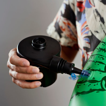 closeup of a young man, wearing a summer shirt, inflating a green pool air mattress with a hand held...