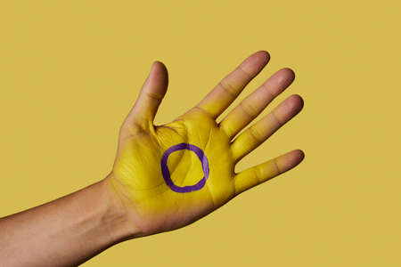 closeup of the intersex flag painted in the palm of the hand of a young person, against a yellow backgroundの写真素材