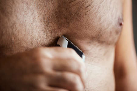 closeup of a young caucasian man in the bathroom trimming the hair of his chest with an electric trimmerの写真素材