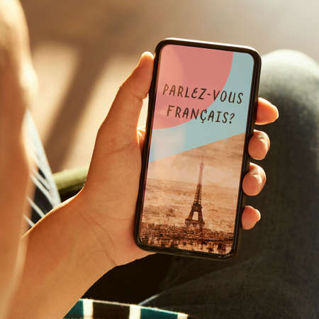 closeup of a young caucasian man, wearing casual clothes, sitting on an armchair, having his smartphone in his hands with the text do you speak French in its screenの写真素材
