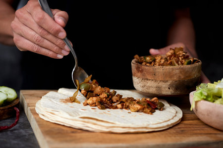 closeup of a young caucasian man preparing a durum or a burrito, with chicken meat cooked with...