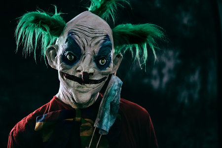 closeup of a disturbing evil clown, with green hair, wearing a dirty red costume and a dirty bow...