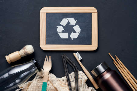 a pile of no-plastic sustainable household items, such as refillable metal and glass bottles, shopping mesh bags, or wooden toiletries, cutlery and chopsticks, and the recycling symbol in a chalkboardの写真素材