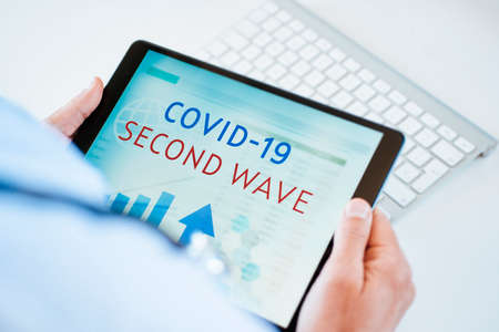 closeup of a doctor man, sitting at his desk, having a digital tablet in his hands with the text covid-19 second wave in its screenの写真素材