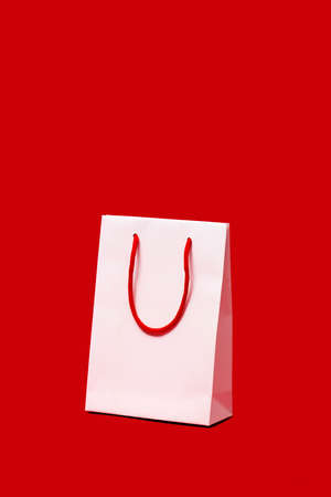 a white paper shopping bag with red handles on a red background, with some blank space on topの写真素材