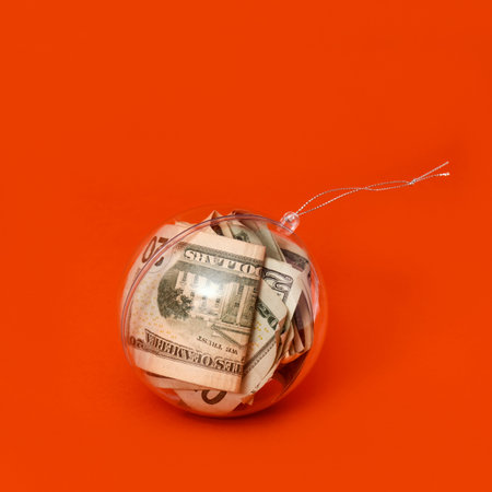 some US dollar banknotes in a clear christmas ball, on an orange background