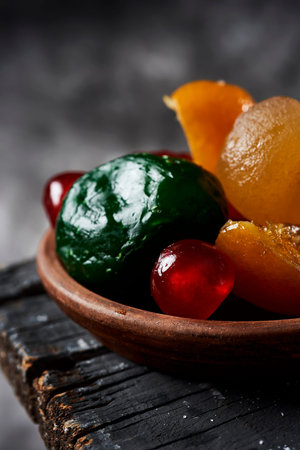 closeup of some appetizing spanish candied fruit, such as orange, pear, plum or maraschino cherries, typically eaten on christmas, on a rustic dark gray wooden surface, against a gray background