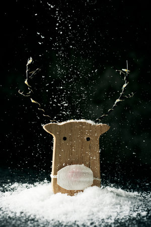 a funny wooden reindeer, wearing a face mask, on the snow while it is snowingの写真素材