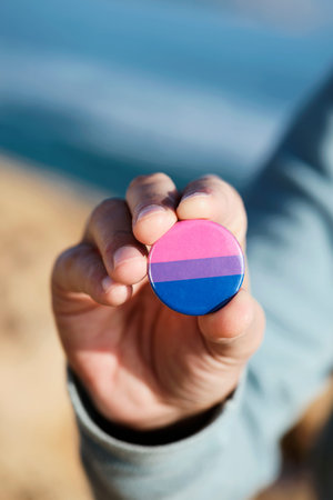 closeup of a young caucasian person outdoors showing a badge patterned with a bisexual pride flag