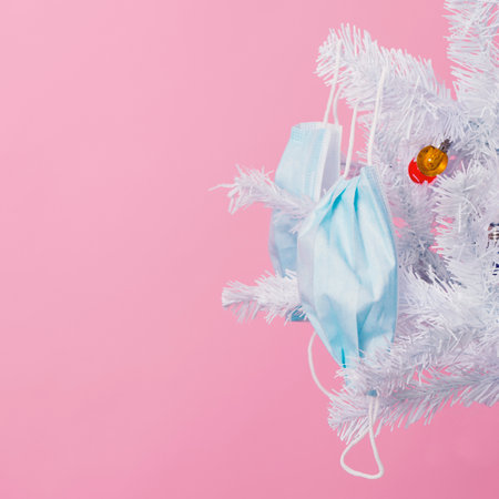 closeup of some blue disposable face masks hanging from the branches of a white christmas tree, against a pink backgroundの写真素材