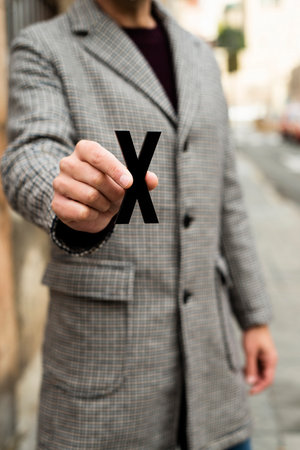 closeup of a young caucasian person standing on the street, wearing a coat, showing an X, for the third gender categoryの写真素材
