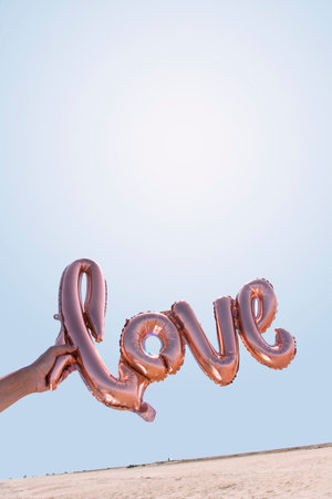 closeup of the hand of a young caucasian man holding a balloon in the shape of the word love against the blue sky, with some blank space on topの写真素材
