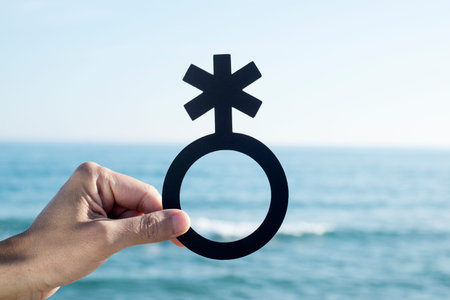closeup of a young caucasian person holding a non-binary gender symbol in front of the oceanの写真素材