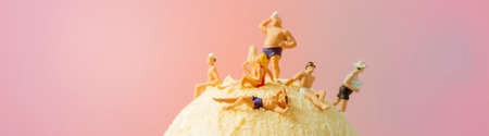 some miniature people, wearing swimsuit, relaxing on top of a vanilla ice cream ball, against a pink background, in a panoramic format to use as web banner or headerの写真素材