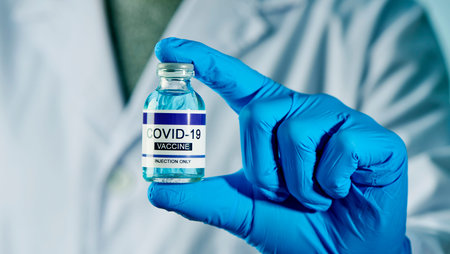 closeup of a healthcare worker man, wearing blue surgical gloves, with a simulated covid-19 vaccine...