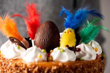 closeup of a young man carrying a spanish mona de pascua, a cake eaten on Easter Monday, ornamented with a chocolate egg, a plush chick and feathers of different colorsの写真素材