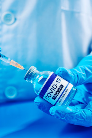 closeup of a healthcare or laboratory worker, wearing blue surgical gloves, filling a syringe from a vial of a simulated covid-19 vaccineの写真素材