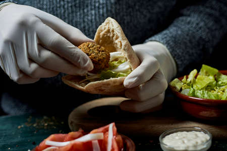 closeup of a young man, wearing latex gloves, preparing a falafel sandwich in a pita breadの写真素材