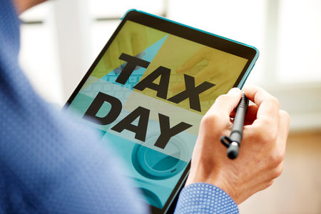 closeup of a young caucasian man, wearing a blue shirt, looking at his tablet, that reads the text tax day in its screenの写真素材