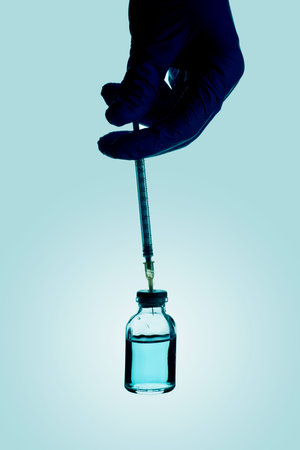 closeup of a healthcare or laboratory worker, wearing surgical gloves, filling a syringe from a vial with a blue liquidの写真素材