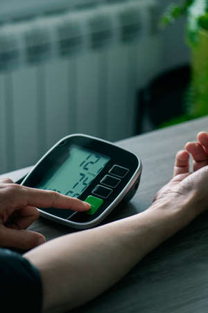 closeup of a caucasian man, sitting at a table, measuring his own blood pressure with an electronic sphygmomanometerの写真素材