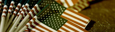 closeup of some flags of the United States of America, attached to wooden poles on a dark surface, in a panoramic format to use as web banner or headerの写真素材