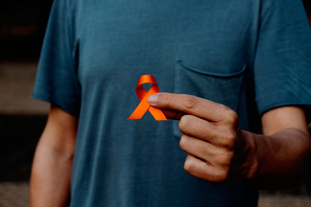 closeup of a young caucasian man, wearing a gray t-shirt, with an orange ribbon in his hand, in...