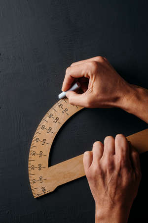 a caucasian man uses a wooden protractor on a dark gray chalkboardの写真素材