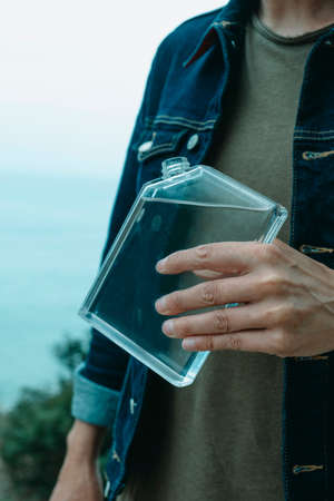 a young man, wearing a denim jacket and a casual green t-shirt, is about to drink from a rectangular reusable water bottleの写真素材